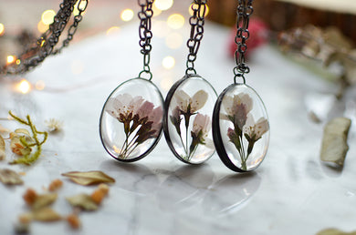 A pendant featuring cherry blossoms preserved in glass (stained glass technique, black patina).