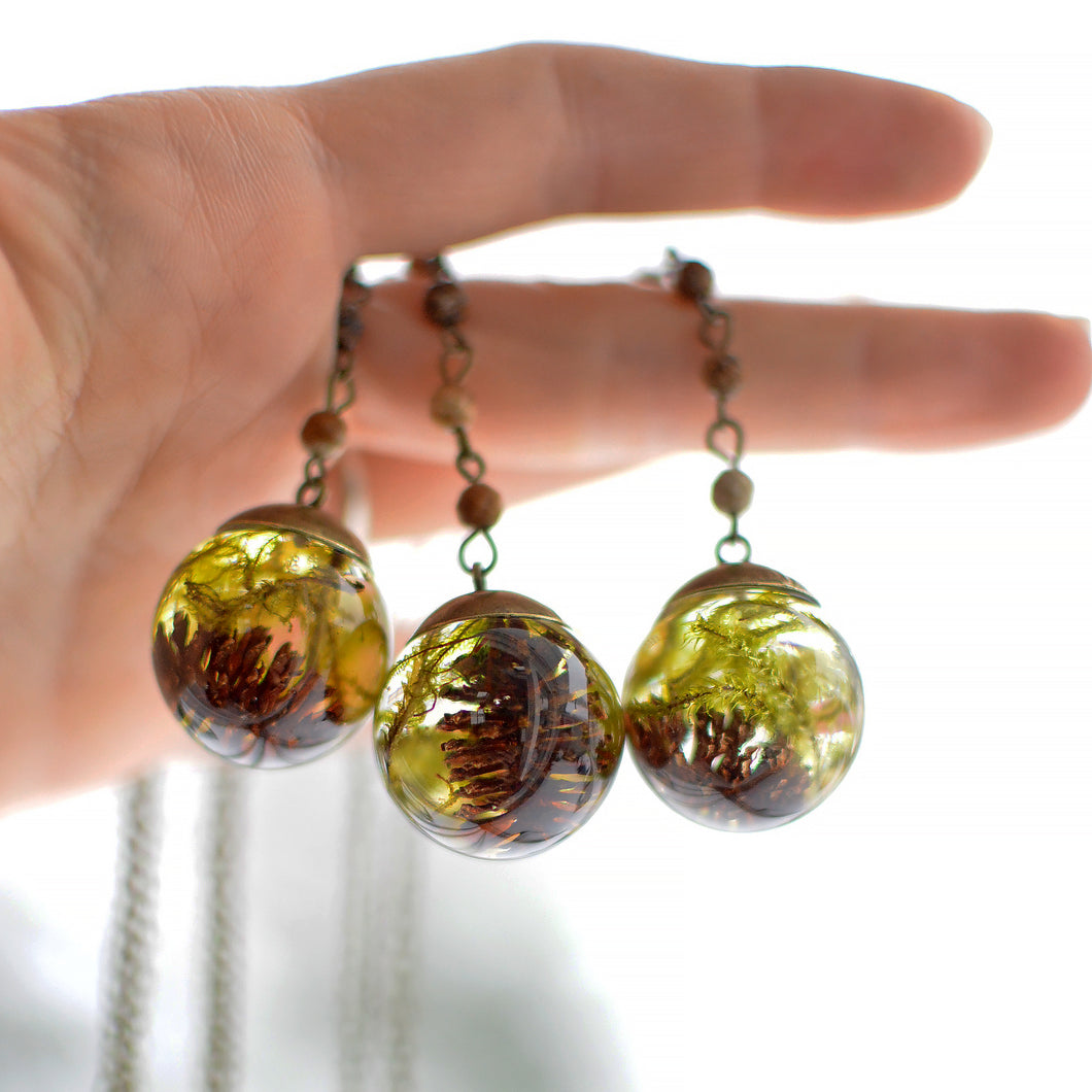  This necklace features preserved moss and a tiny alder pinecone forever suspended in the clear eco-resin. The sphere is complemented with a brass top and comes on 25 inches brass chain, adorned with small natural jaspers.   The sphere measures about 1 inch in diameter.